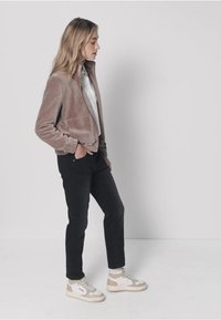 Veste courte marron clair à la texture douce, portée sur un haut blanc, associée à un jean noir et des baskets beige, présentée sur un fond neutre.