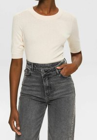 Maglione corto a maniche corte di colore crema chiaro con scollo rotondo, abbinato a jeans in denim grigio scuro a vita alta, leggermente usurati.