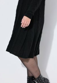 Abito nero lavorato a maglia con motivo a treccia, maniche lunghe e polsini a coste, indossato con collant neri trasparenti e stivaletti alla caviglia con borchie.