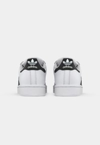 White Adidas sneakers viewed from the back, featuring black heel tabs with the Adidas trefoil logo and brand name.