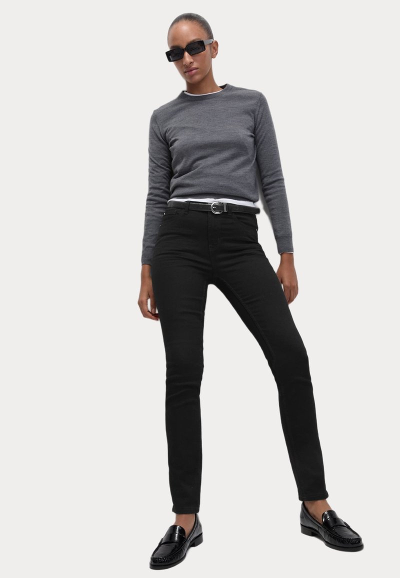 Μαύρο στενό τζιν παντελόνι συνδυασμένο με γκρι μακρυμάνικο τοπ. Το σύνολο διαθέτει μια λευκή ζώνη και μαύρες λοφέρες. Τα γυαλιά ηλίου ολοκληρώνουν την εμφάνιση.