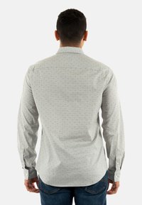 Chemise à manches longues gris clair avec un petit motif de pois sombres, poignets à boutons et un ourlet légèrement incurvé. Design de col classique.