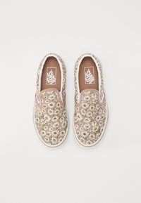 Blomstrete slip-on sko med et beige lerstoff, dekorert med hvite tusenfryd og grønne accenter, med en hvit gummisåle og brun innersåle.