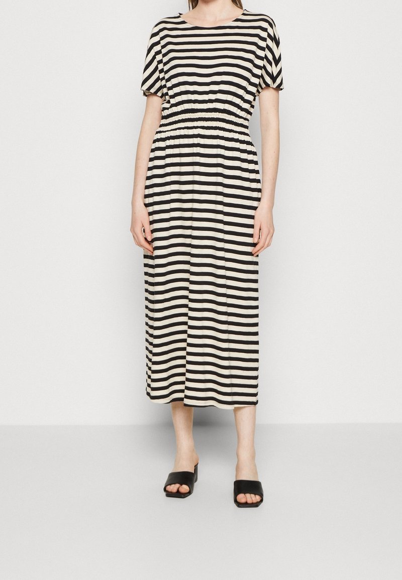 Raitapaitainen midi-mekko vaniljanvärisenä ja mustana, jossa on lyhyet hihat ja koolla kerätty vyötärö. Pehmeä kangas, rento malli, yhdistettynä mustiin liukuvasti sujautettaviin sandaaleihin.