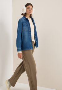 Camicia di jeans blu intenso, maglione in maglia crema sotto, pantaloni larghi color khaki e cuffie in pelliccia sintetica bianca, indossati con sneaker beige.