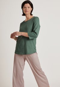 Top verde a maniche lunghe con scollatura rotonda; abbinato a pantaloni larghi rosa a fantasia con un motivo a diamante. Tessuto morbido, vestibilità casual.