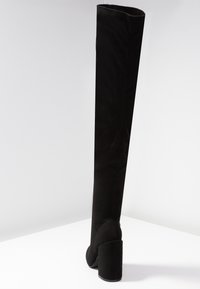 Bota negra por encima de la rodilla en suave tela con tacón cuadrado. Presenta un diseño elegante y liso con puntera redondeada y un caña alta.
