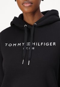 Schwarzes Sweatshirt aus Baumwollmischung mit Kordelzügen und silbernen Spitzen. Mit weißem "TOMMY HILFIGER"-Logo und Gründungsjahr.