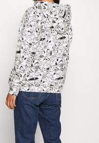 Felpa con cappuccio bianca con un motivo di cartoni animati neri che rappresenta sport e personaggi. Realizzata in tessuto morbido, con una vestibilità rilassata e maniche lunghe.