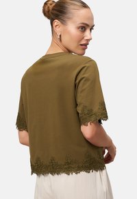 Olive green short-sleeve top with lace trim at sleeves and hem, featuring a relaxed fit and smooth fabric texture.