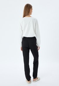 Top blanco de manga larga, corte relajado, combinado con pantalones negros de cintura elástica. Textura suave, diseño fluido, y se lleva con zapatillas de color claro.