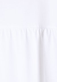 Vit tyg med rynkad sömdetalj som skapar en subtil volangtextur över den mellersta sektionen.