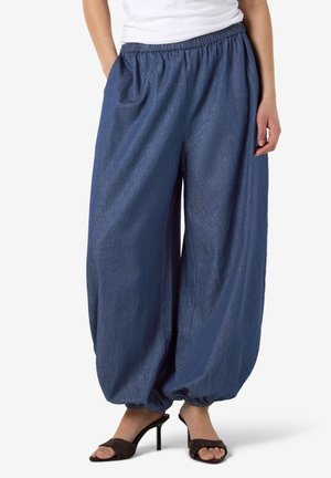 Personne portant un pantalon bleu foncé ample à taille élastique avec chevilles serrées et des sandales noires à talons hauts et bouts ouverts.