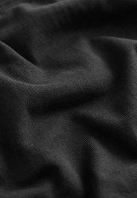 Čierna bavlnená tkanina s hladkou textúrou, viditeľným vzorom väzby a prirodzeným prehýbaním. Povrch vykazuje jemné vrásky a záhyby.