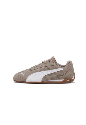Niski beżowy zamszowy sneaker z białym paskiem z logo Puma, brązową gumową podeszwą i wiązaniem na sznurowadła, pokazany z zewnętrznej strony.