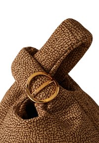 Braune, strukturierte Tasche mit einer samtweichen Oberfläche, einem runden, goldenen Hardware-Akzent und einem markanten Muster. Der Griff ist gepolstert und weich.