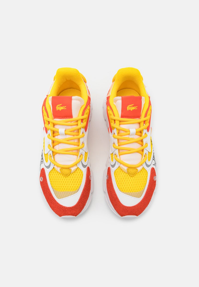 Sneaker colorati con mesh giallo, accenti in suede rosso, sovrapposizioni in pelle bianca e lacci gialli prominenti con un logo sulla linguetta.
