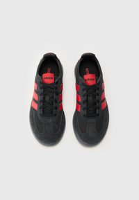 Black athletic shoes with red accents, featuring three stripes, lace-up design, suede and synthetic materials, and textured soles.