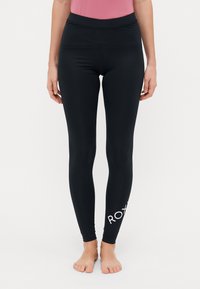 Leggings neri realizzati in materiale elastico, con una vita alta e un logo bianco sulla parte bassa della gamba. Texture liscia e design aderente.