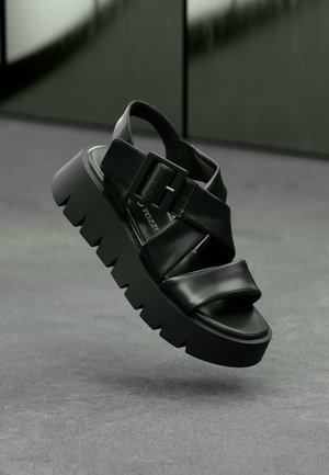 Crni sandali na platformu s širokim trakama, kvadratnom kopčom i debelim, rebrastim potplatom. Glatki materijal s sjajnim završetkom.