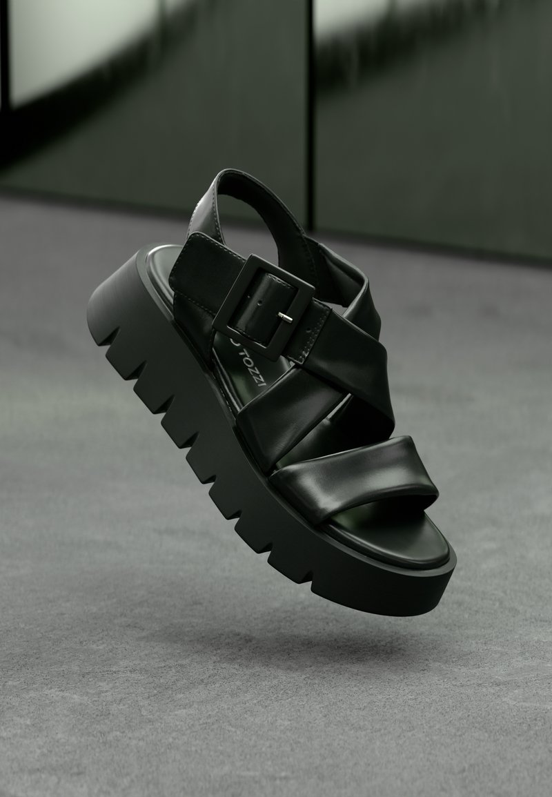 Sandale noire à plateforme avec des larges lanières, une boucle carrée et une semelle épaisse et crantée. Matériau lisse avec une finition brillante.