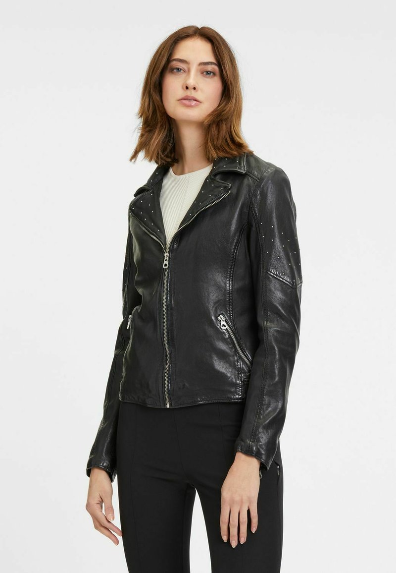 Giacca da moto in pelle nera con borchie argentate sulle spalle, chiusura con zip asimmetrica e due tasche con zip. Tessuto liscio.