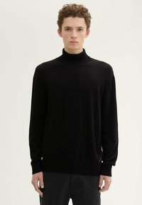 Schwarzer Rollkragenpullover, gestrickte Textur, lange Ärmeln und gerippte Bündchen und Saum. Besitzt eine lockere Passform und seitliche Schlitze am Saum.
