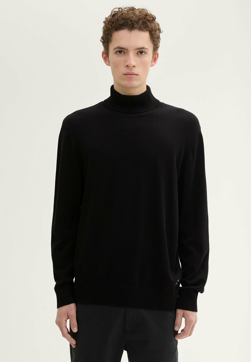 Schwarzer Rollkragenpullover, gestrickte Textur, lange Ärmeln und gerippte Bündchen und Saum. Besitzt eine lockere Passform und seitliche Schlitze am Saum.