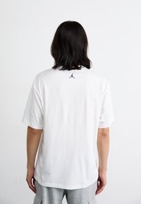 Hvid T-shirt med korte ærmer lavet af bomuld, med et lille sort Jordan-logo på den øverste ryg. Casual pasform med et enkelt design.