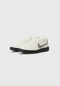 White sneakers with black rubber soles, smooth leather and fabric upper, featuring a grey Nike swoosh and lace-up design.