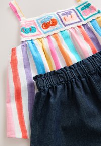 Striped sleeveless top with colorful embroidery at the neckline; paired with dark denim shorts featuring an elastic waistband.