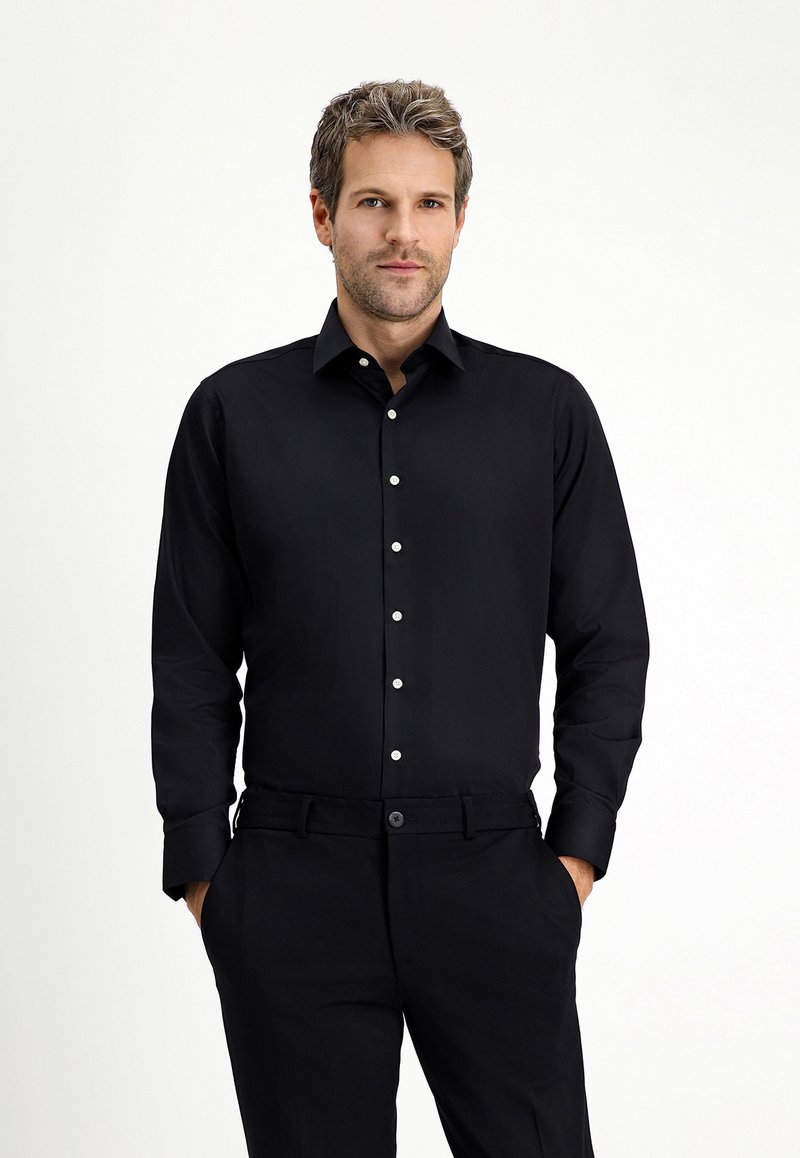 Zwarte lange mouwen shirt met een slim fit, voorzien van een puntige kraag en witte knopen aan de voorkant, gecombineerd met zwarte broek.