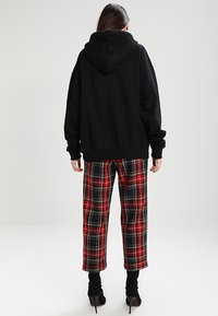 Czarna, oversize bluza z kapturem, zestawiona z szerokimi spodniami w czerwono-czarną kratę. Gładka tekstura materiału i luźny krój.