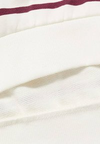 Vit tyg med en ribbad textur, prydd med ett vinrött rand högst upp och en meshpanel längst ner med en slät söm.
