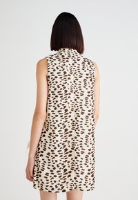 Vestido sin mangas en una tela beige con estampado de animal en negro y marrón. El diseño incluye una costura sutil en la parte trasera y un suave drapeado.