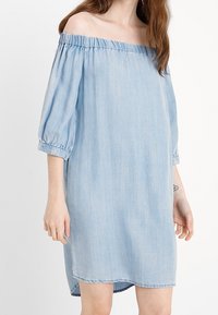 Světle modré šaty bez ramínek vyrobené z denimové látky, s tříčtvrtečními nabíranými rukávy a rovný střih, který má mírně zakřivený lem.