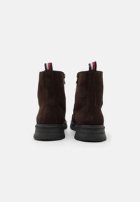 Botines de ante marrón con suelas de goma negra. La parte trasera cuenta con un cierre de cremallera y una lengüeta de tres colores. Logo de la marca grabado en la suela.