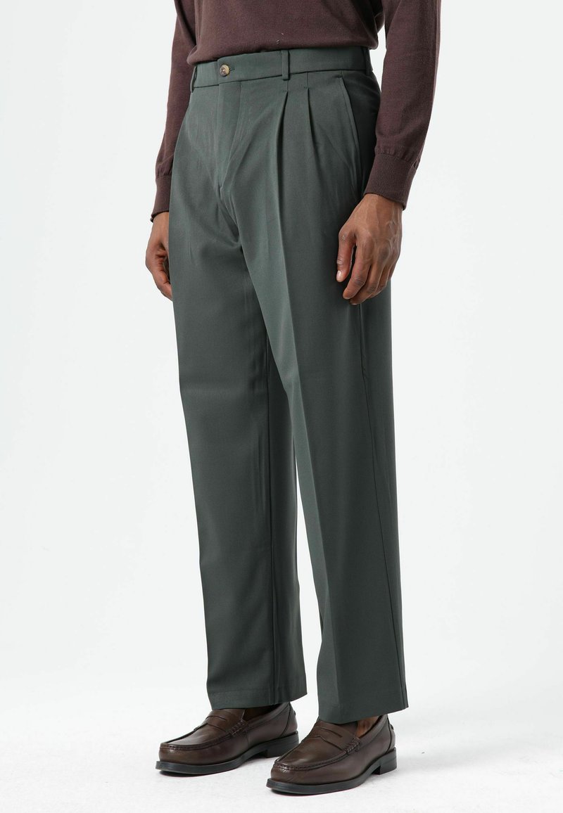 Groene geplooide broek met knoopsluiting, voorzien van een rechte pijp en een gladde textuur, gecombineerd met bruine loafers.