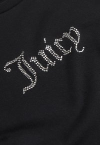 Črn material bluze z besedo "Juicy" v srebrnih kamenčkih, z gladko teksturo in krojnim izrezom.