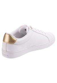 Białe sneakersy z gładką syntetyczną cholewką, płaską gumową podeszwą i złotym akcentem na pięcie. Mają sznurowaną konstrukcję i minimalne szwy.