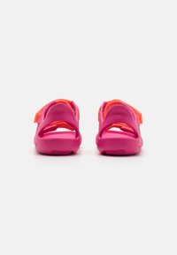 Pink sandals with a textured surface, an adjustable orange strap, and an open back design. Features a thick sole for comfort.