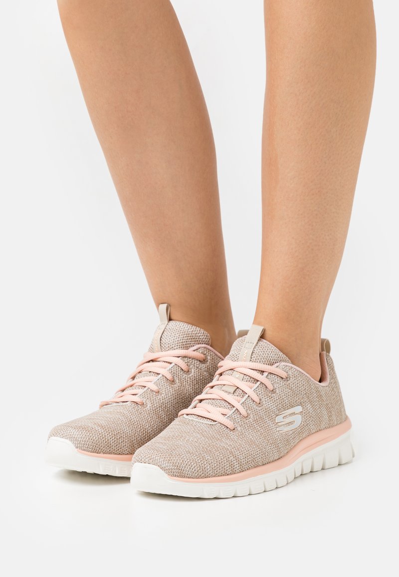 Lekki obuwie sportowe wykonane z beżowej siateczki z różowymi akcentami. Posiada textured cholewkę, okrągły czubek, płaską białą podeszwę oraz sznurowanie.