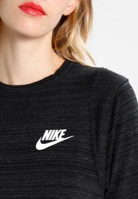 Svart Nike-tröja med en strukturerad tygkvalitet, rund hals och vit logga som är tydligt synlig på bröstet. Slät, lätt material.