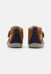 Smeđe antilop čizme s mornarsko plavim detaljima, okrugli vrh, podesiva traka i gumeni đon. Sadrže logotip i mekanu podstavu za udobnost.