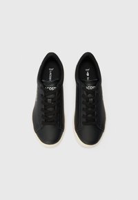 Sneakers in pelle nera con una texture liscia, dotati di lacci neri, suola color crema e un accento del logo verde.