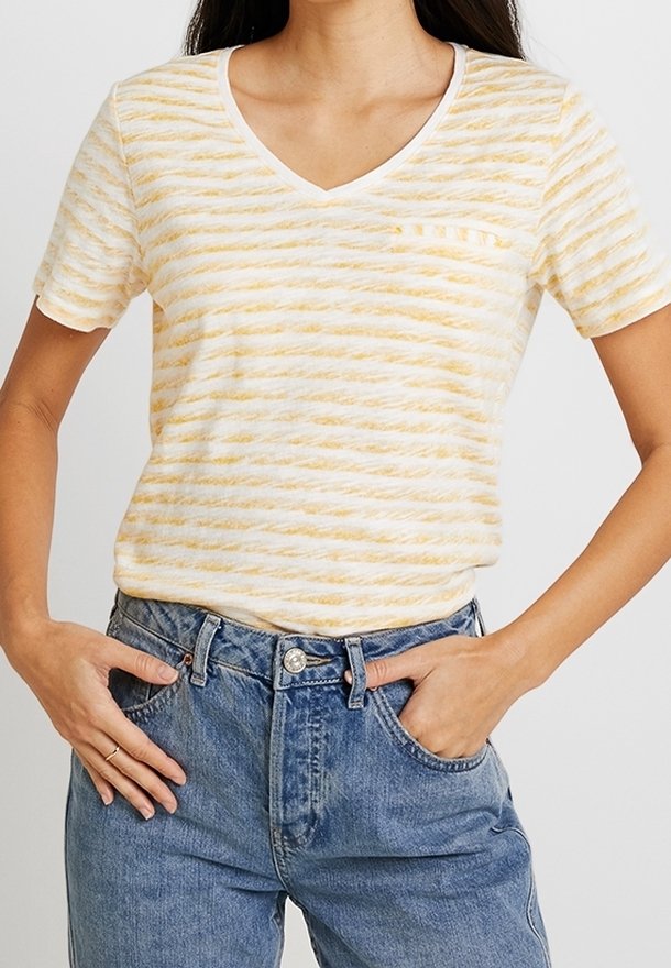 Camiseta de algodón a rayas amarillas y blancas con escote en V, mangas cortas y un bolsillo en el pecho izquierdo, combinada con jeans de tiro alto azules.