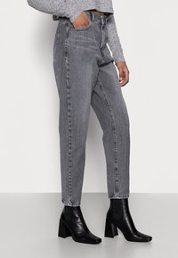 Högmidjade, rakbenade jeans i ett urtvättat grått denim. Har sidofickor och dragkedja. Matchas med svarta ankelstövlar.