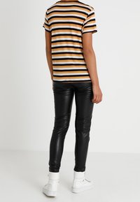 Pruhované tričko v oranžové, černé a bílé, spárované s dobře padnoucími černými koženými kalhotami a bílými vysokými teniskami.