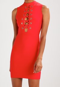 Ärmlös klädd röd klänning med hög halsringning och korslagd snörning framtill, med en figursyd hos knäet.