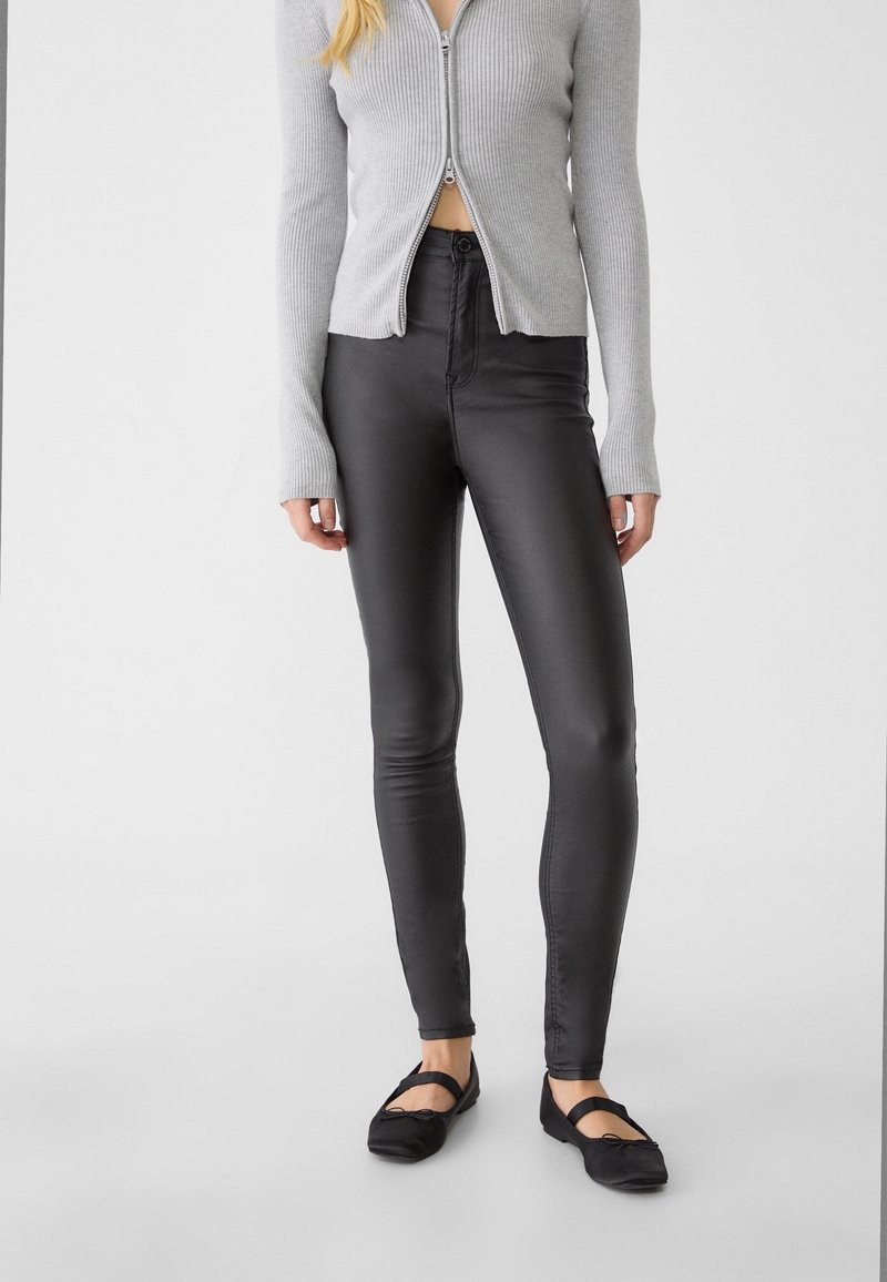 Leggings noirs et brillants en matière extensible, avec une taille haute et une coupe ajustée, associés à un cardigan zippé côtelé gris.